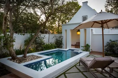 an infinity pool with an umbrella next to a house at Akademie Street Boutique Hotel in Franschhoek