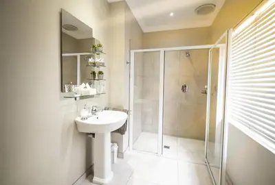 a white bathroom with a shower and a sink at Oak Tree Lodge in Paarl