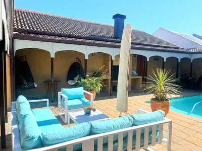 a patio with a couch and a umbrella and a pool at On The Cliff Guest House in Hermanus