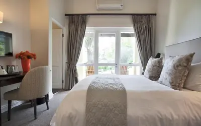 a bedroom with a bed and a desk and a window at Sugarbird Manor in Stellenbosch