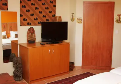 a room with a television on a cabinet with a bed at Golf and Garden Guesthouse in Somerset West