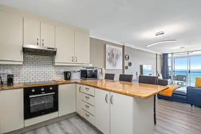 a kitchen with white cabinets and a living room at The Waves 1002 in Bloubergstrand