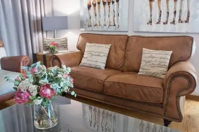 a brown couch sitting in a living room with flowers at Avemore Wag n Bietjie No 1 in Stellenbosch