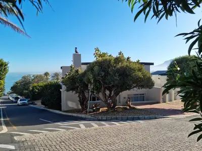 a building with a tree on the side of a street at 'Die Braaihuis'- sleeps 6, Large Veranda, Sea Views, Central and Fabulous! in Gordonʼs Bay