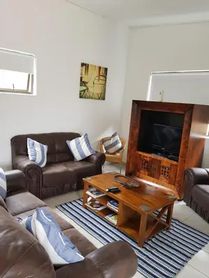 a living room with couches and a tv and a table at Stukkie Cottage in Hermanus