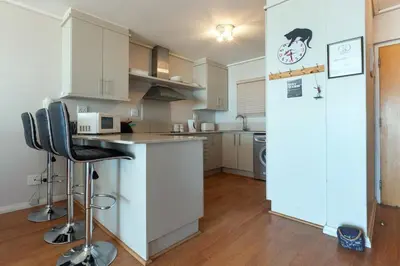 a kitchen with white cabinets and a counter and a refrigerator at Lagoon Beach 136A by CTHA in Cape Town