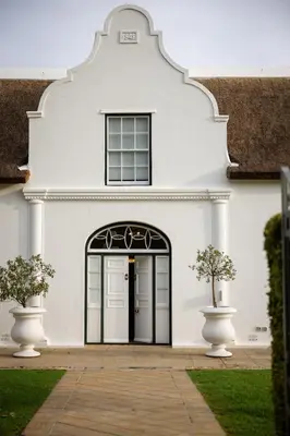 a white house with a black door and two vases at Allèe Bleue Wine Estate in Simondium