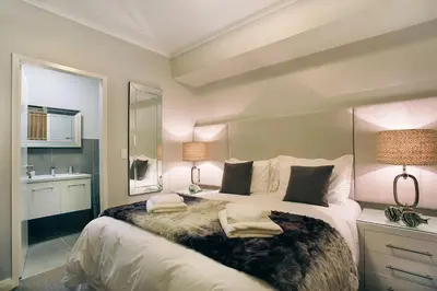 a bedroom with a large bed with two lamps and a sink at Superior Apartment Mayfair in Cape Town