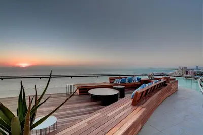 a wooden deck with benches and tables on the beach at Ocean View Penthouse in Strand
