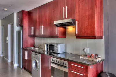 a kitchen with red wooden cabinets and a microwave at Portico 802 in Bloubergstrand
