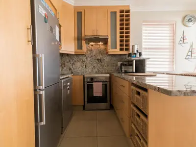 a kitchen with wooden cabinets and a stainless steel refrigerator at 'The View' on Bikini Beach, Seafront, 2 bedroom, Sleeps 4 in Gordonʼs Bay