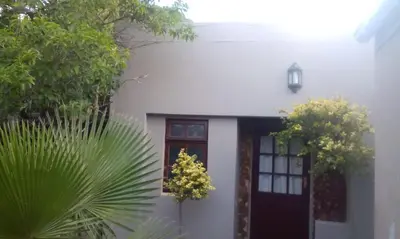 a white house with a black door and trees at The Buddha Garden in Cape Town