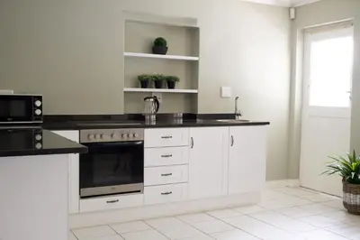 a kitchen with white cabinets and black counter tops at Laurel Cottage in Franschhoek