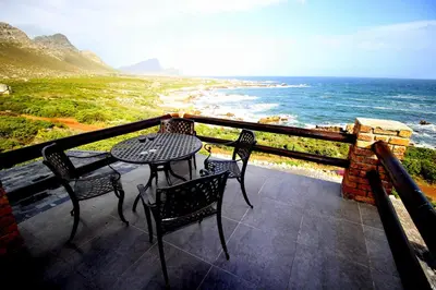a table and chairs on a balcony overlooking the ocean at Proteus Beach House in Rooiels