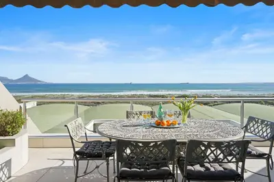 a table on a balcony with a view of the ocean at Dolphin Beach H106 in Bloubergstrand