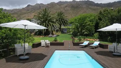 a swimming pool with two umbrellas and a deck with at Bloemenzee Boutique B&B in Gordonʼs Bay