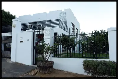 a white house with a black gate and a plant at Paarl Mountain Lodge in Paarl