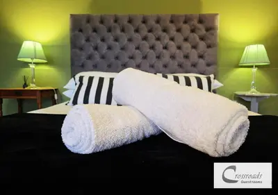 a bed with white towels on it with two lamps at Crossroads Guestrooms in Gordonʼs Bay