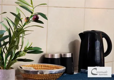 a table with a black coffee pot and a plant at Crossroads Guestrooms in Gordonʼs Bay