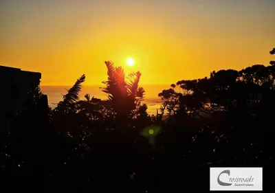 a sunset over the ocean with trees in the foreground at Crossroads Guestrooms in Gordonʼs Bay