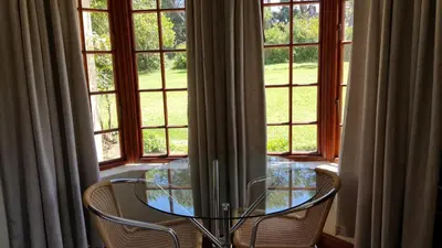 a glass table and two chairs in front of a window at Tuckaway in Somerset West