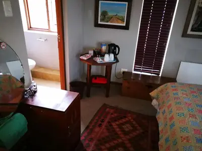 a bedroom with a bed and a table with a chair at Die Pastorie in Caledon