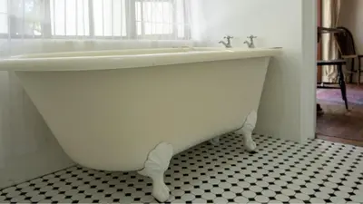 a white bath tub in a bathroom with a black and white floor at Eastcliff Cottage in Hermanus