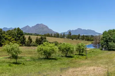 a field with trees and a river and mountains at Wildlife Retreat on a Wine-Farm in Stellenbosch