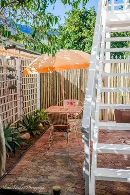 a patio with an orange umbrella and a table with a ladder at Cobie Apartment in Stellenbosch