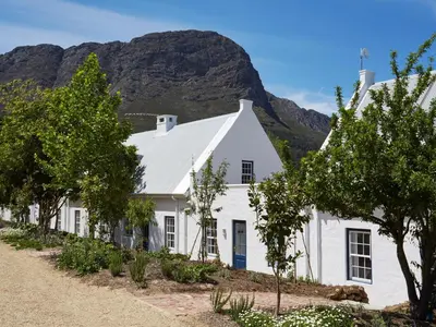 a white house with a mountain in the background at La Cotte Forest Cottages in Franschhoek