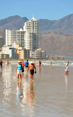 a group of people walking in the water on a beach at Pebble Moon Holiday Flat in Strand