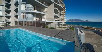 a swimming pool in front of a building with the ocean at Horizon Bay 1404 by HMH in Bloubergstrand
