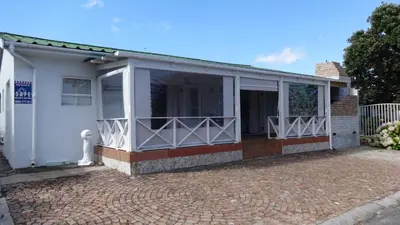 a white house with a dog standing in front of it at Leisure By The Sea in Kleinmond