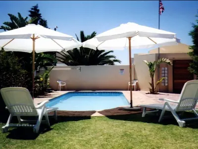 a swimming pool with two chairs and two umbrellas at Blue Mountain Guest House in Bloubergstrand