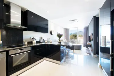 a kitchen with black cabinets and a living room at Lux Andringa Walk Apartments in Stellenbosch