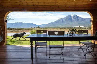 a table and chairs on a porch with a dog in the distance at The Riverstone House in Romansrivier