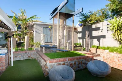 a backyard with a stone retaining wall and a table and a ping at Strand Guesthouse in Strand