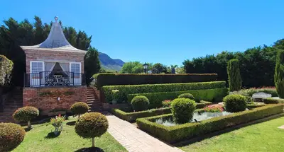 a garden with hedges and a building with a fountain at Villa Adalbert Guesthouse in Somerset West