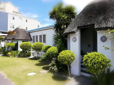 a white house with a thatched roof and a yard at Dolphin Inn Blouberg in Bloubergstrand