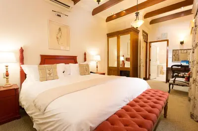 a bedroom with a large white bed with a red bench at Coopmanhuijs Boutique Hotel & Spa in Stellenbosch