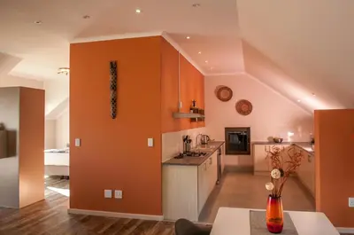 a kitchen with an orange wall and a counter at Wind-Rose Guest House in Gordonʼs Bay