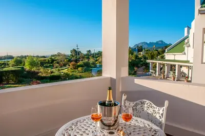 a table with a bottle of wine and glasses on a balcony at Wind-Rose Guest House in Gordonʼs Bay