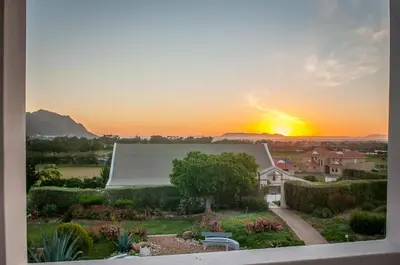 a view of a house with the sunset in the background at Wind-Rose Guest House in Gordonʼs Bay