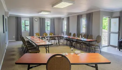 a dining room with tables and chairs and windows at Ruslamere Hotel and Conference Centre in Durbanville