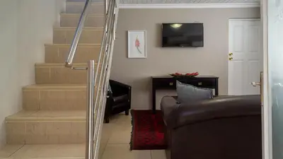 a living room with a couch and stairs with a television at Ruslamere Hotel and Conference Centre in Durbanville