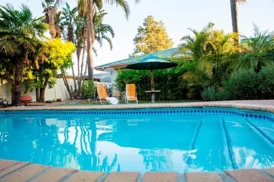 a swimming pool with a table and an umbrella at Eikepark Self Catering in Stellenbosch