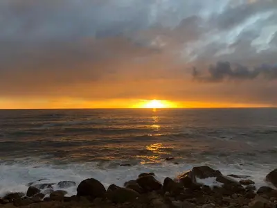 a sunset over the ocean with rocks in the water at da Heim Guest House in Cape Town