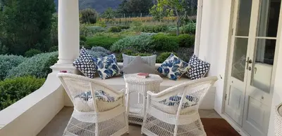 a porch with white wicker chairs and pillows at La Cotte House in Franschhoek