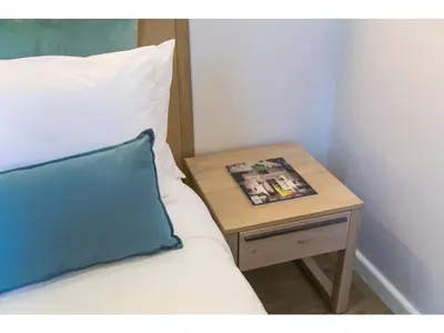a bed with a side table with a blue pillow and a magazine at Eikehoff Apartments in Stellenbosch