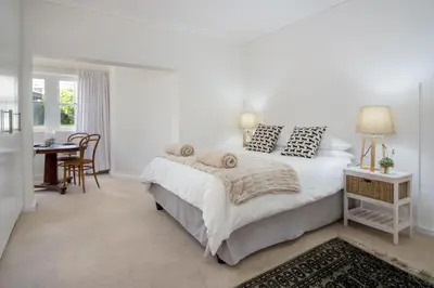 a white bedroom with a bed and a table at Stone Chimney Cottage in Hermanus